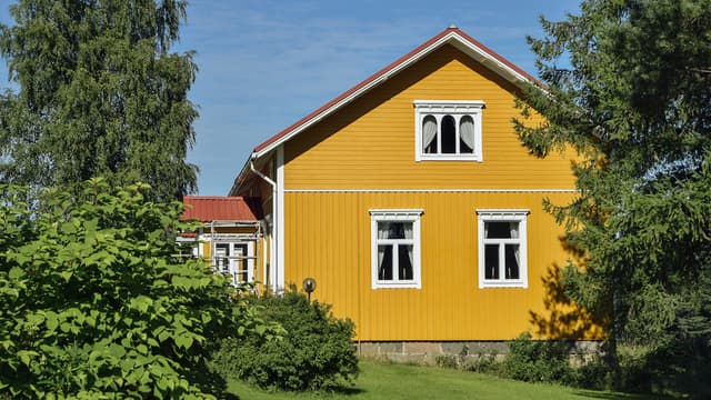 Keltainen omakotitalo kesäisessä pihassa